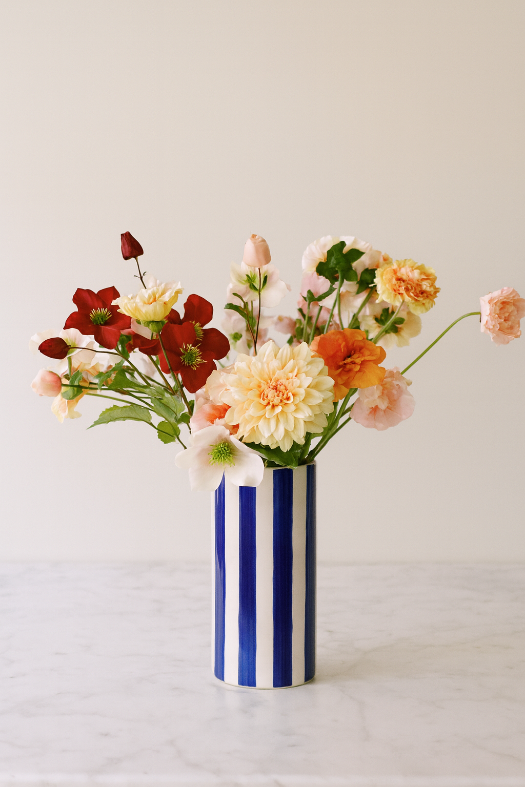 Composition Studio XL — dahlia crème, hellébore, clématite dans vase bleu rayé
